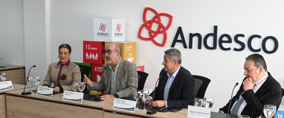 Cuatro personas están sentadas en una mesa; tres hablan y una observa. Al fondo, aparece el logo de Andesco
