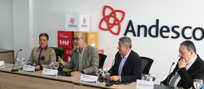Cuatro personas están sentadas en una mesa; tres hablan y una observa. Al fondo, aparece el logo de Andesco