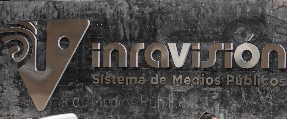 Cartel metálico sobre fondo gris oscuro, con un logotipo y el texto "Sistema de Medios Públicos"