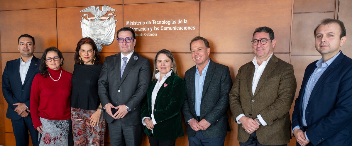 Ocho personas posan de pie ante una pared de madera con emblema y texto del Ministerio de Tecnologías de la Información y las Comunicaciones