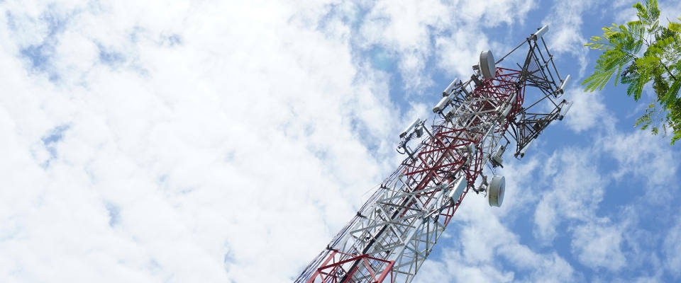 Torre metálica de telecomunicaciones inclinada hacia la esquina superior derecha, con antenas y cielo azul con nubes.