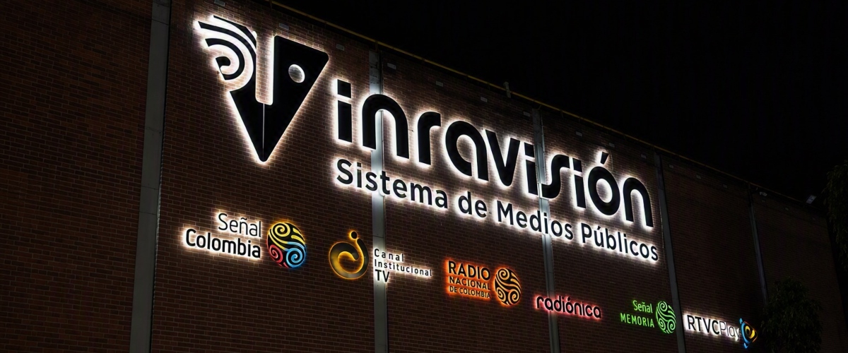 Fachada de ladrillo con letrero iluminado de RTVC Sistema de Medios Públicos y varios logotipos.