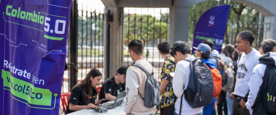 Personas hacen fila junto a una mesa con equipos tecnológicos. Un pendón de Colombia 5.0 aparece a la izquierda.