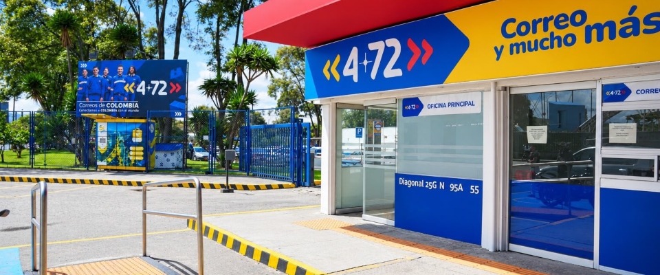 Oficina de 4-72 con fachada azul, amarilla y roja; al frente hay rampas, barandas y zonas ajardinadas.