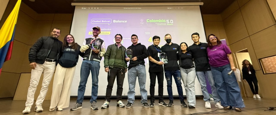 Nueve personas posan en un escenario frente a una pantalla con información de Colombia 5.0; algunas sostienen reconocimientos. Nueve personas posan en un escenario frente a una pantalla con información de Colombia 5.0; algunas sostienen reconocimientos.