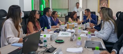 Personas reunidas alrededor de una mesa, conversan y revisan documentos.